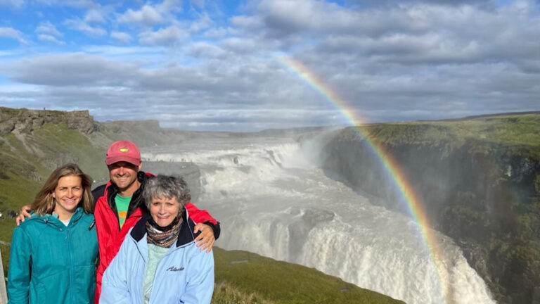 Picture of tourists at Gullfoss Waterfall in sunny day. Rainbow visible over the waterfall and group of tourist in a far distance.