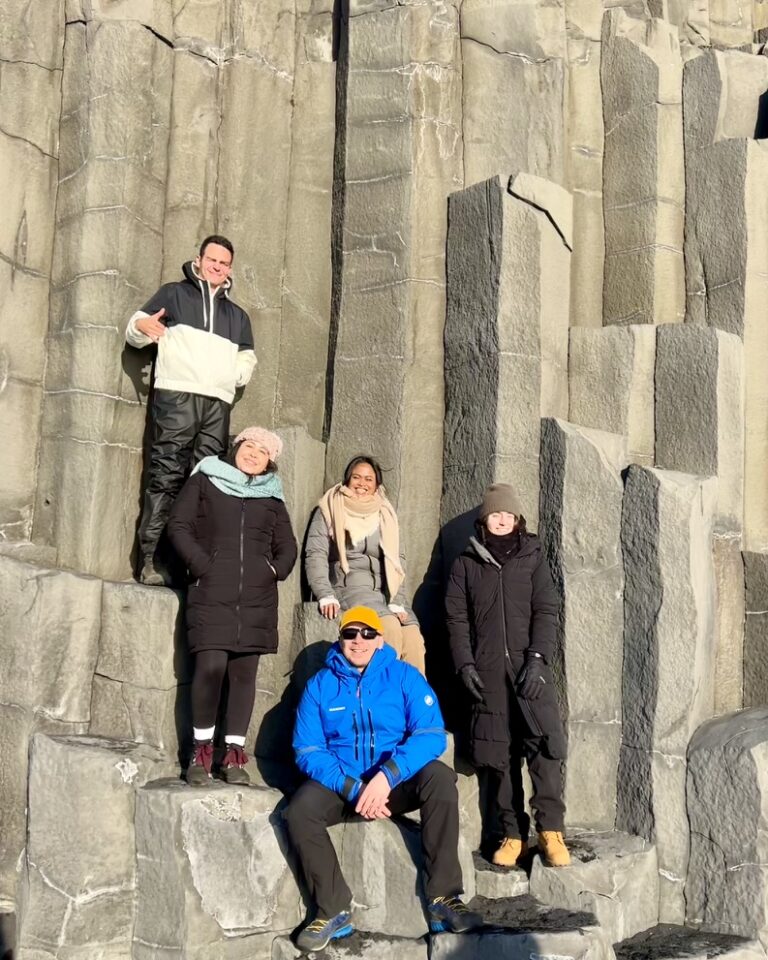 A group of tourists with a guide by the basalt columns at the Reynisfjara black sand beach in Iceland.