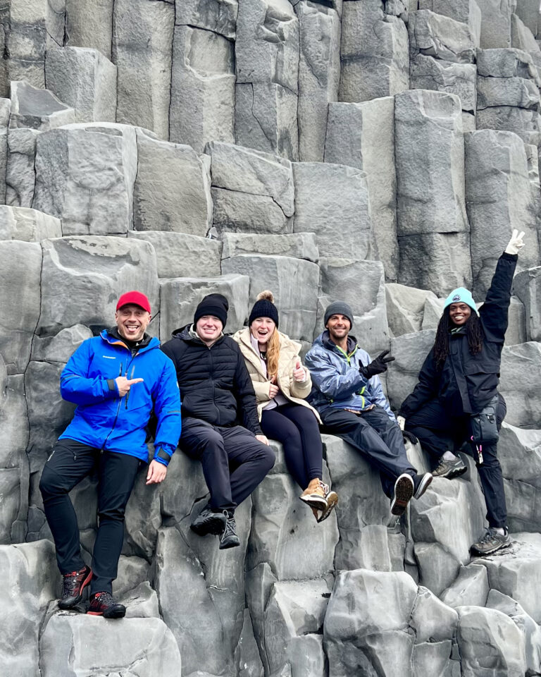 A group of tourists with a guide by the basalt columns at the Reynisfjara black sand beach in Iceland.