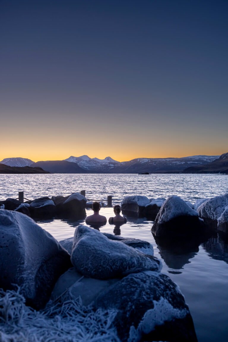 Picture of a couple relaxing at the Hvammsvik hot spring during a wintry sunset.